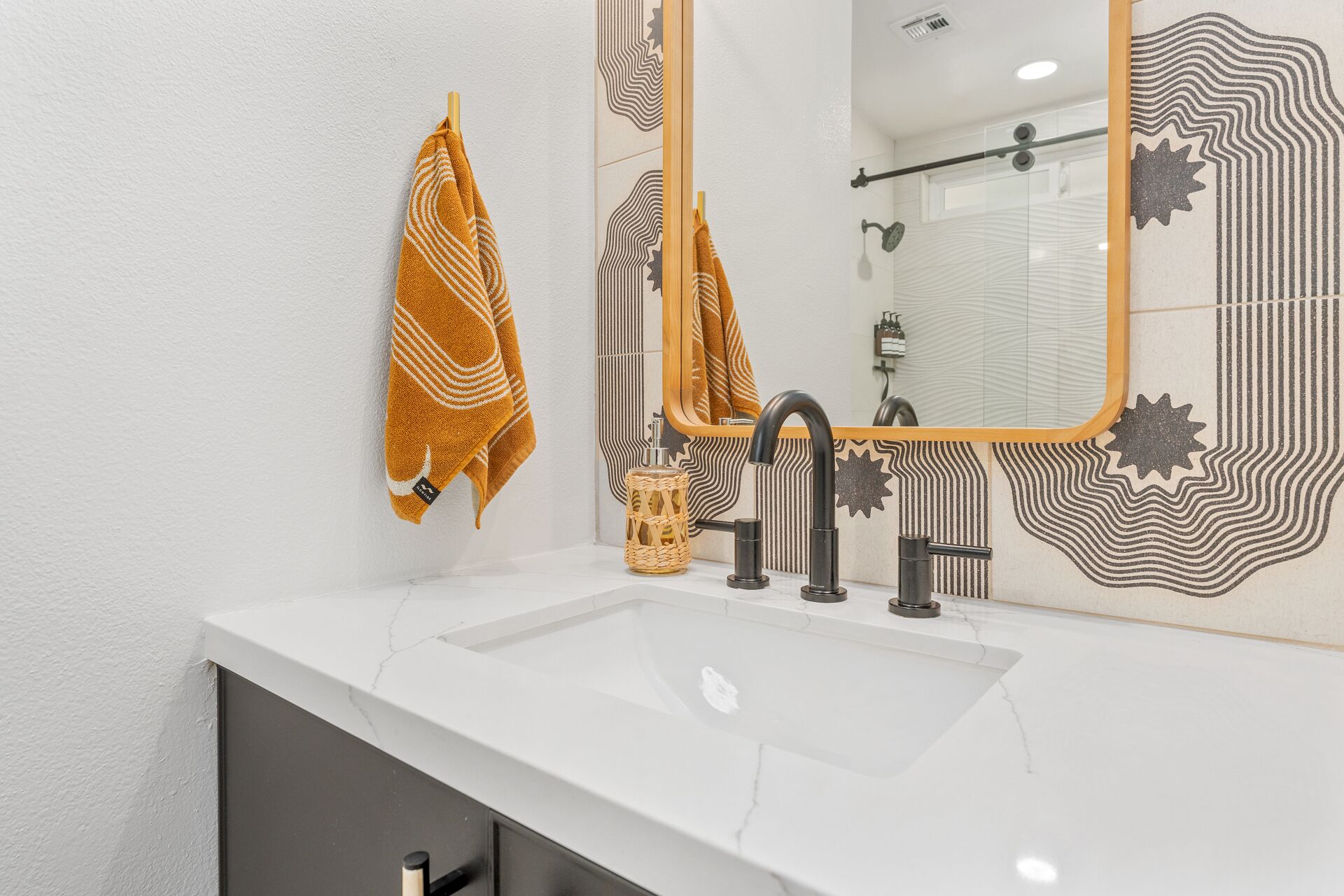 A bathroom with a white sink, black faucet, and a mirror with a geometric pattern.