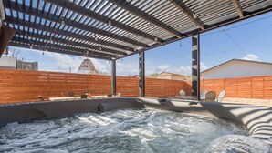 A hot tub with a wooden deck and a metal roof, surrounded by a wooden fence and a brick wall.