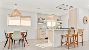 A modern kitchen with a dining area, featuring a central island, wooden chairs, and a hanging light fixture.