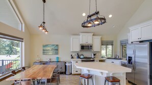 Una cocina moderna con armarios blancos, electrodomésticos de acero inoxidable, una mesa de comedor de madera y una isla grande con taburetes.