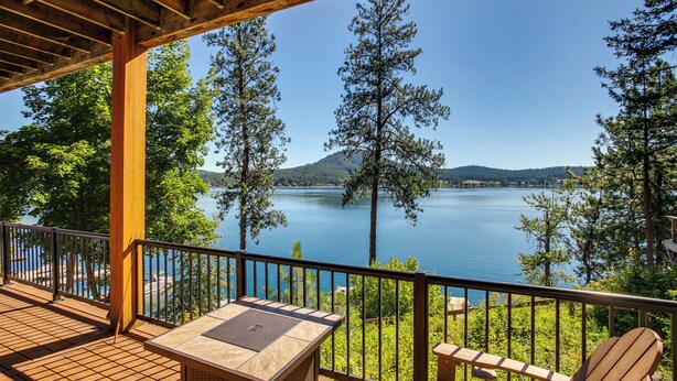 Terraza de madera con mesa y sillas con vista a un lago rodeado de árboles.