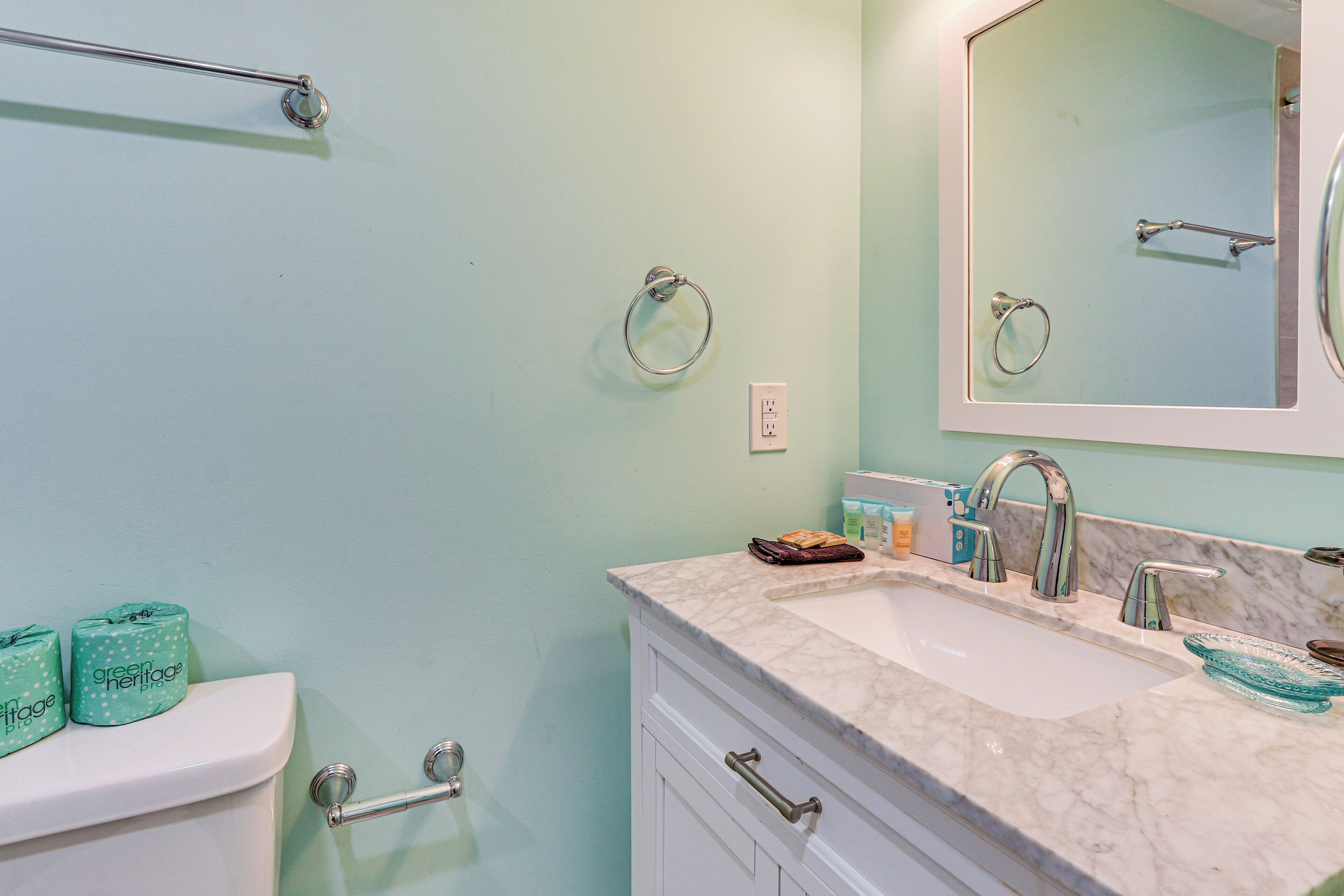 A bathroom with a toilet, sink, and mirror. There are toilet paper rolls, a towel, and a soap dish on the sink counter.