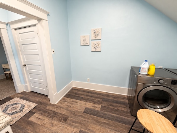 A laundry room with a washing machine, a wooden chair, and a rug on the floor.