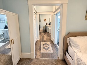 A hallway leading to a bedroom with a bed, a kitchen area, and a bathroom visible through an open door.