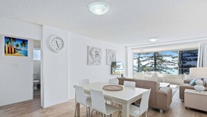 A modern living room with a dining area, white furniture, and artwork on the walls. - Goodwin Towers 10, Burleigh Heads. (Gold Coast)