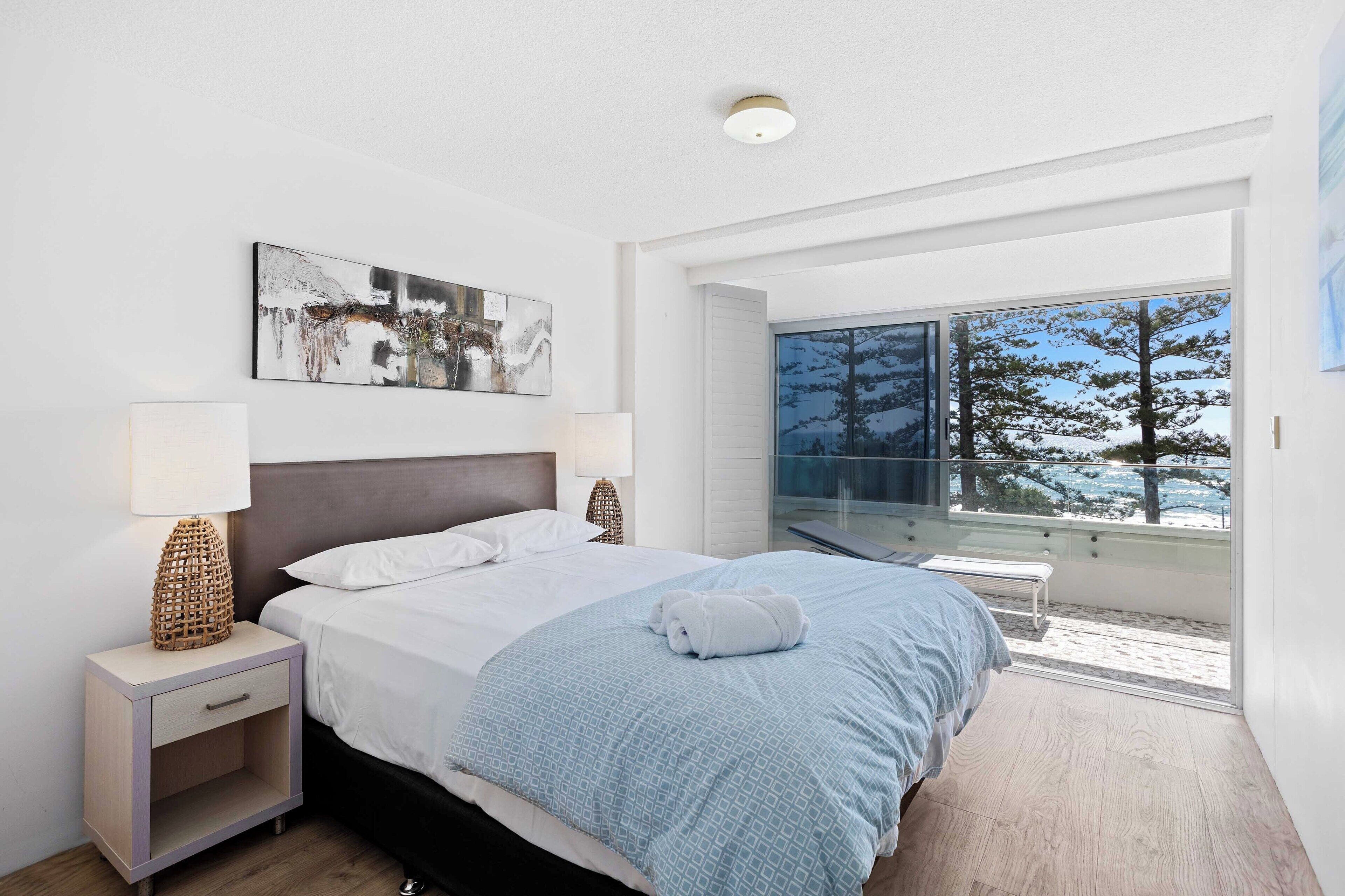 Een moderne slaapkamer met een groot bed, een nachtkastje met een lamp, en uitzicht op een besneeerd landschap door een groot raam.