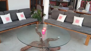 Un salon moderne avec deux canapés gris, chacun agrémenté d’un coussin blanc orné d’un motif géométrique rouge. Une table basse en verre, dotée d’un pied en bois original, se trouve au centre de la pièce.