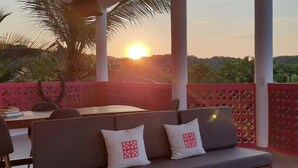 Une terrasse avec un canapé et une table, offrant une vue panoramique et un magnifique coucher de soleil.