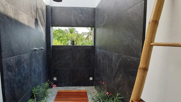 Une salle de bain moderne avec des carreaux de couleur sombre, un banc en bois et une petite fenêtre donnant sur un espace verdoyant.