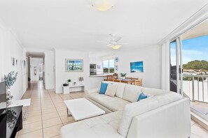 Relax in a spacious living area with a sofa, coffee table, and flat-screen TV, plus a balcony with a hillside view.