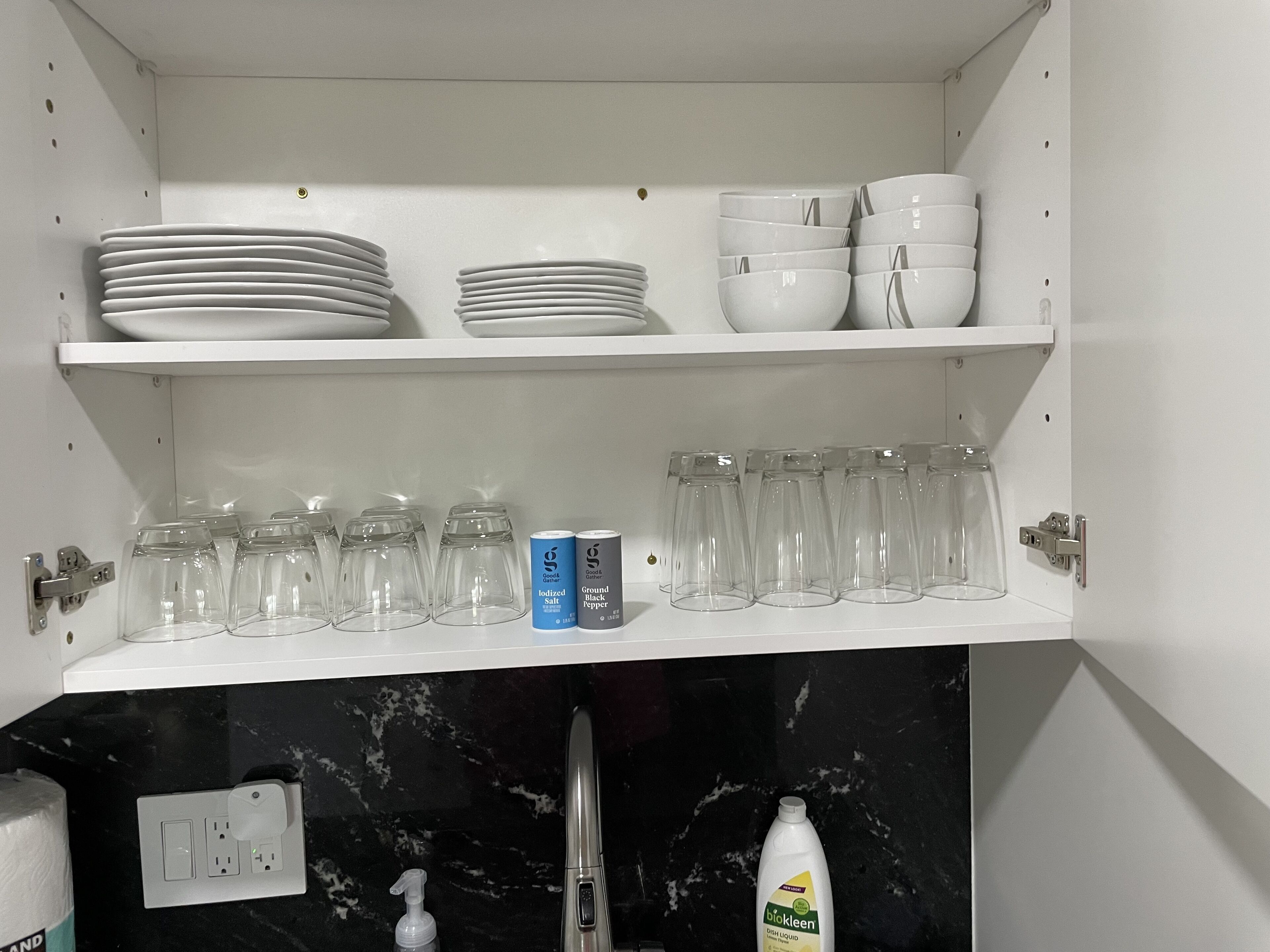 Un meuble de cuisine avec des étagères blanches où sont rangées des assiettes, des bols et des verres.