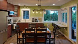 Une cuisine moderne avec des meubles en bois, une table à manger avec des chaises, un four encastré et une fenêtre donnant sur un espace verdoyant.