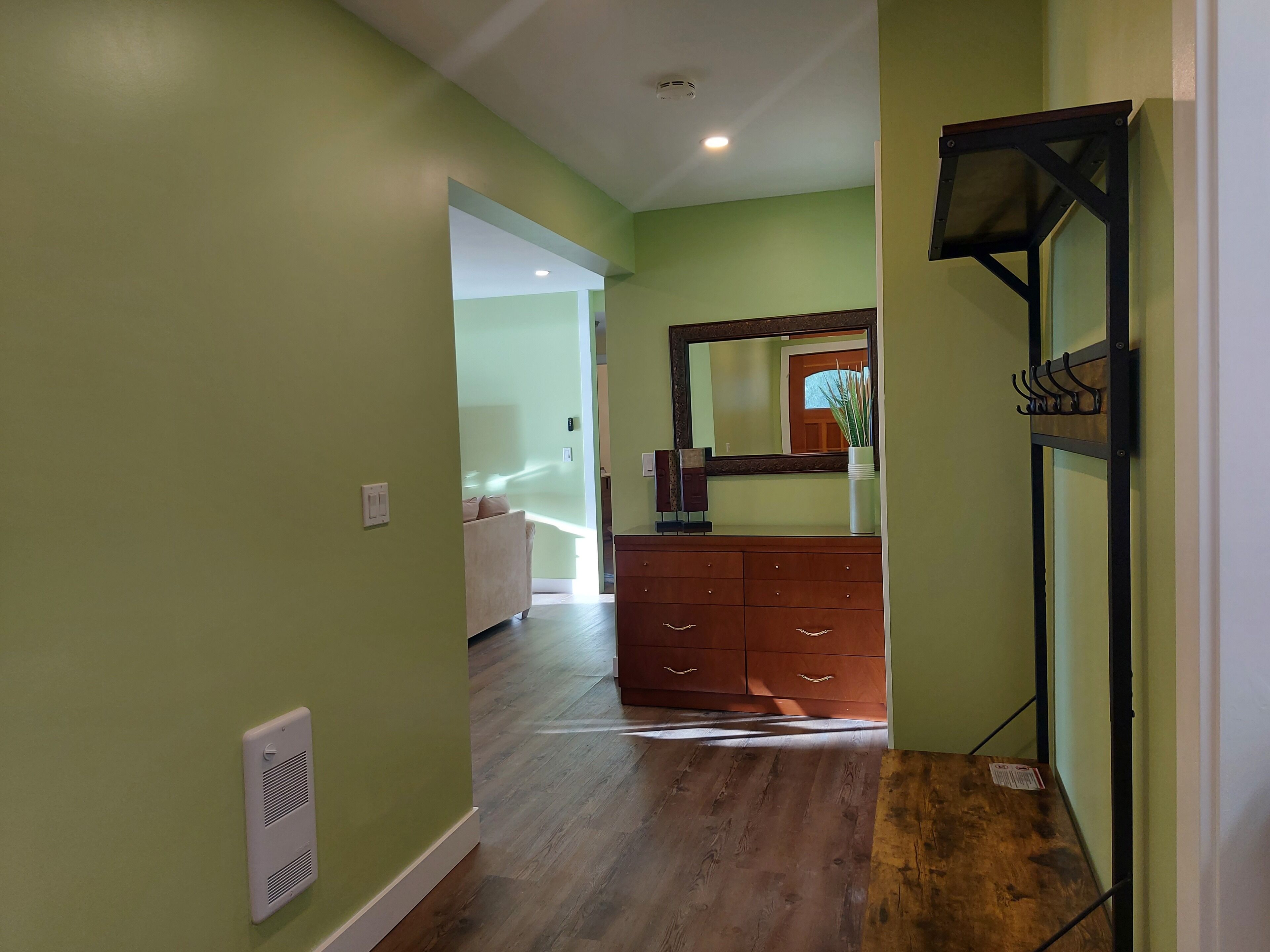 Un couloir avec un plancher en bois, une commode en bois, un miroir et un radiateur fixé au mur.