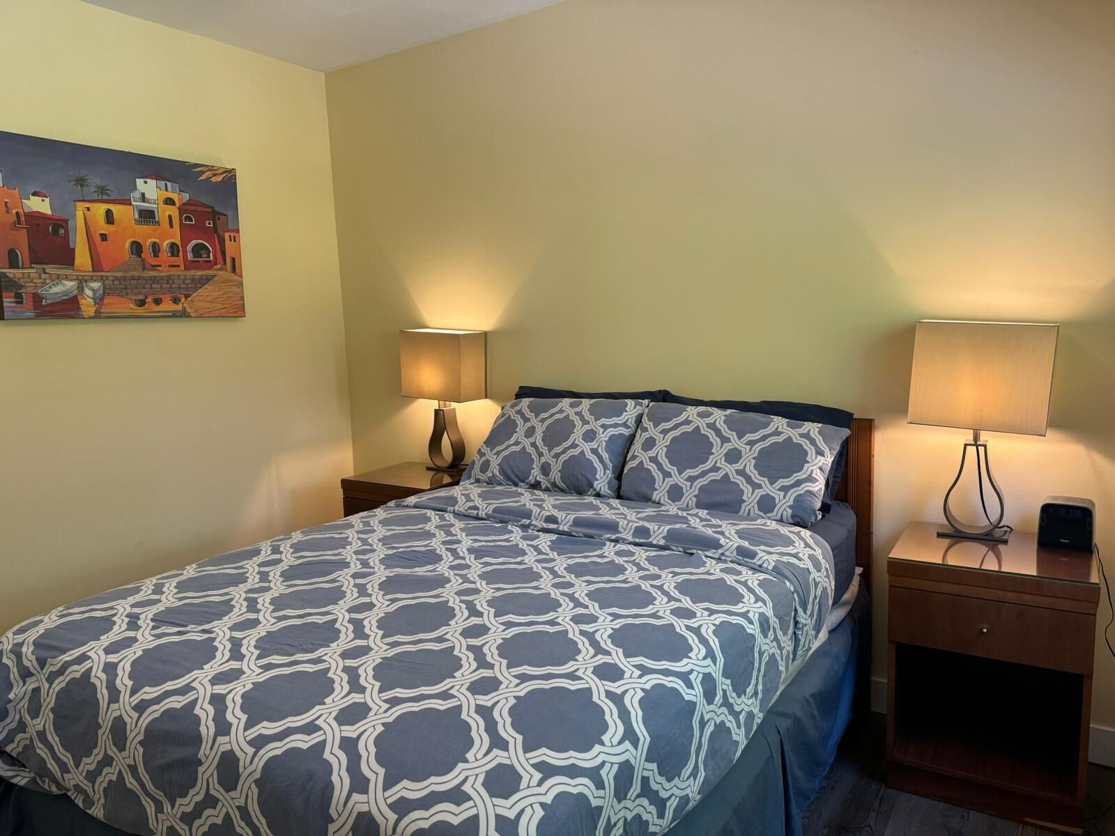 Een hotelkamer met een bed, twee nachtkastjes en een schilderij aan de muur.