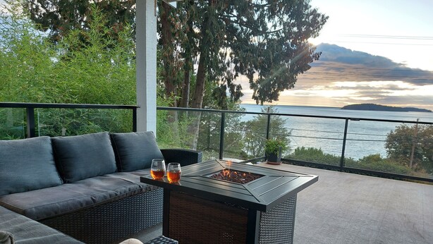 Un balcon avec un canapé et une table, donnant sur une étendue d’eau et des arbres.