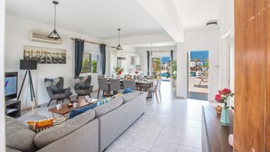 A spacious living area with a sofa, chairs, a dining table, and a TV. - Protaras Fig Tree Bay Villa Jv4 (Paralimni)