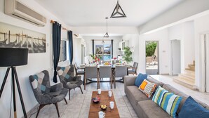 A modern living room with a dining area, a sofa set, and a coffee table. - Protaras Fig Tree Bay Villa Jv4 (Paralimni)