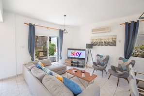 A modern living room with a sofa, armchairs, a coffee table, and a TV displaying the word 'sky'. - Protaras Fig Tree Bay Villa Jv4 (Paralimni)