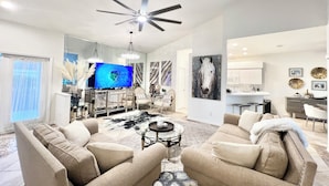 A modern living room with a ceiling fan, a flat-screen TV, and a dining area with a kitchen in the background. - Exclusive Lely Resort House -Private Pool -Sleeps 6 (Naples)