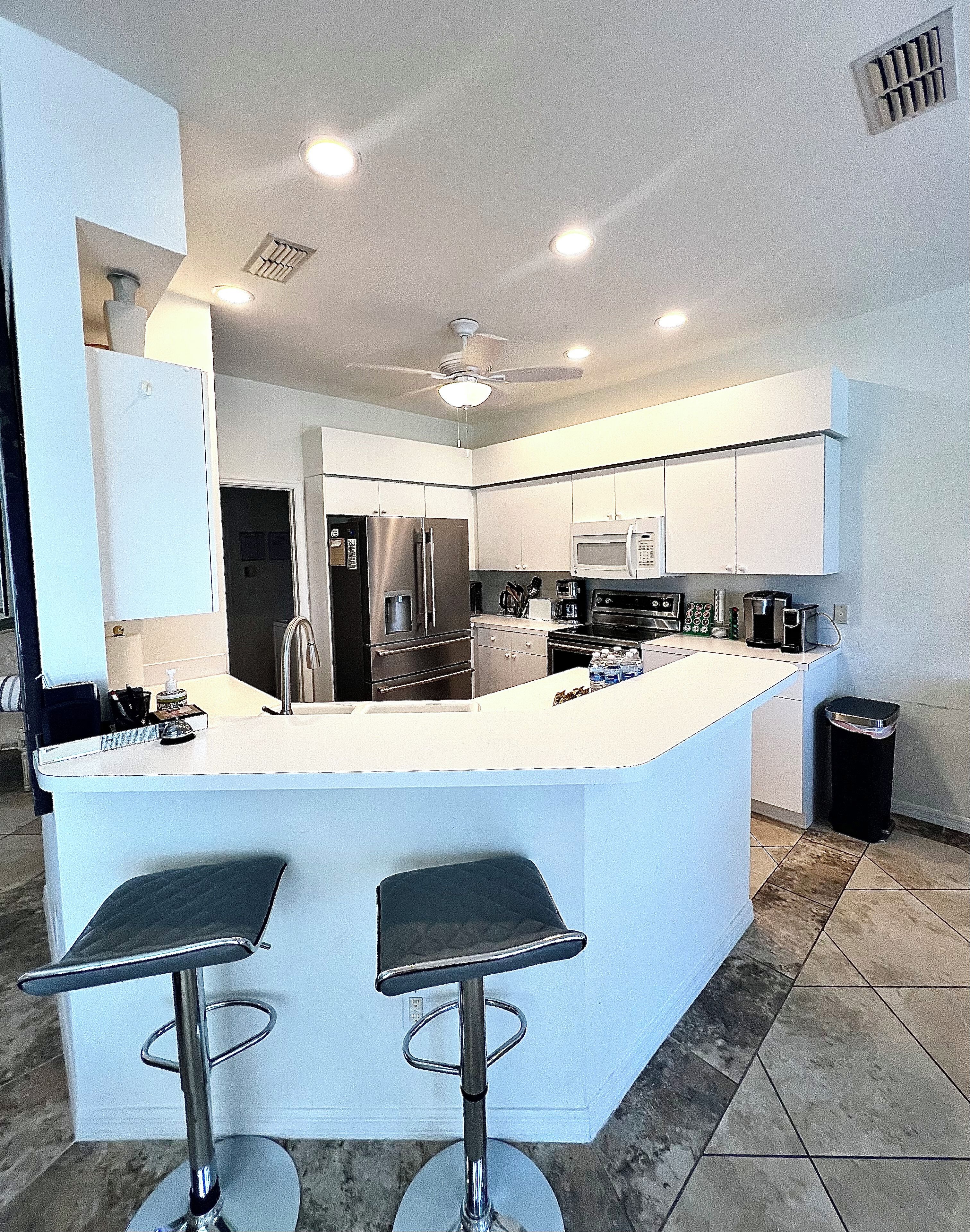 A modern kitchen with a central island, stainless steel appliances, and a ceiling fan.