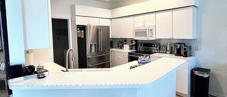 A modern kitchen with a central island, stainless steel appliances, and a ceiling fan.