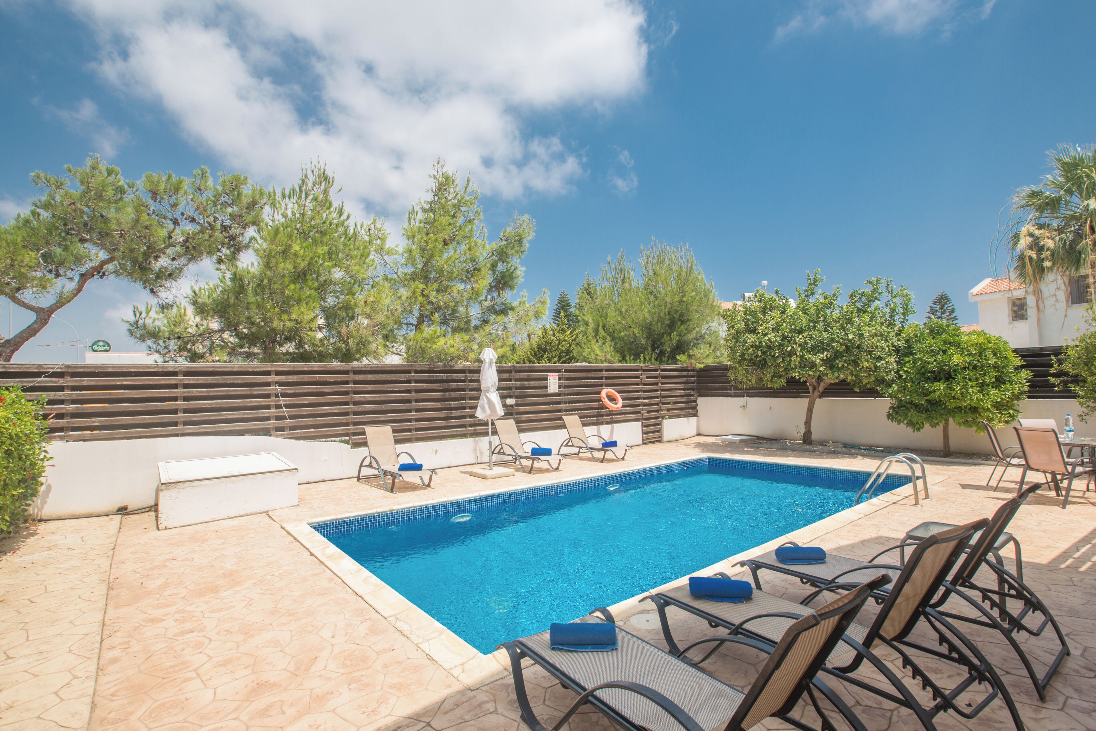 Une piscine rectangulaire aux carreaux bleus, entourée de chaises longues et d’une petite table.