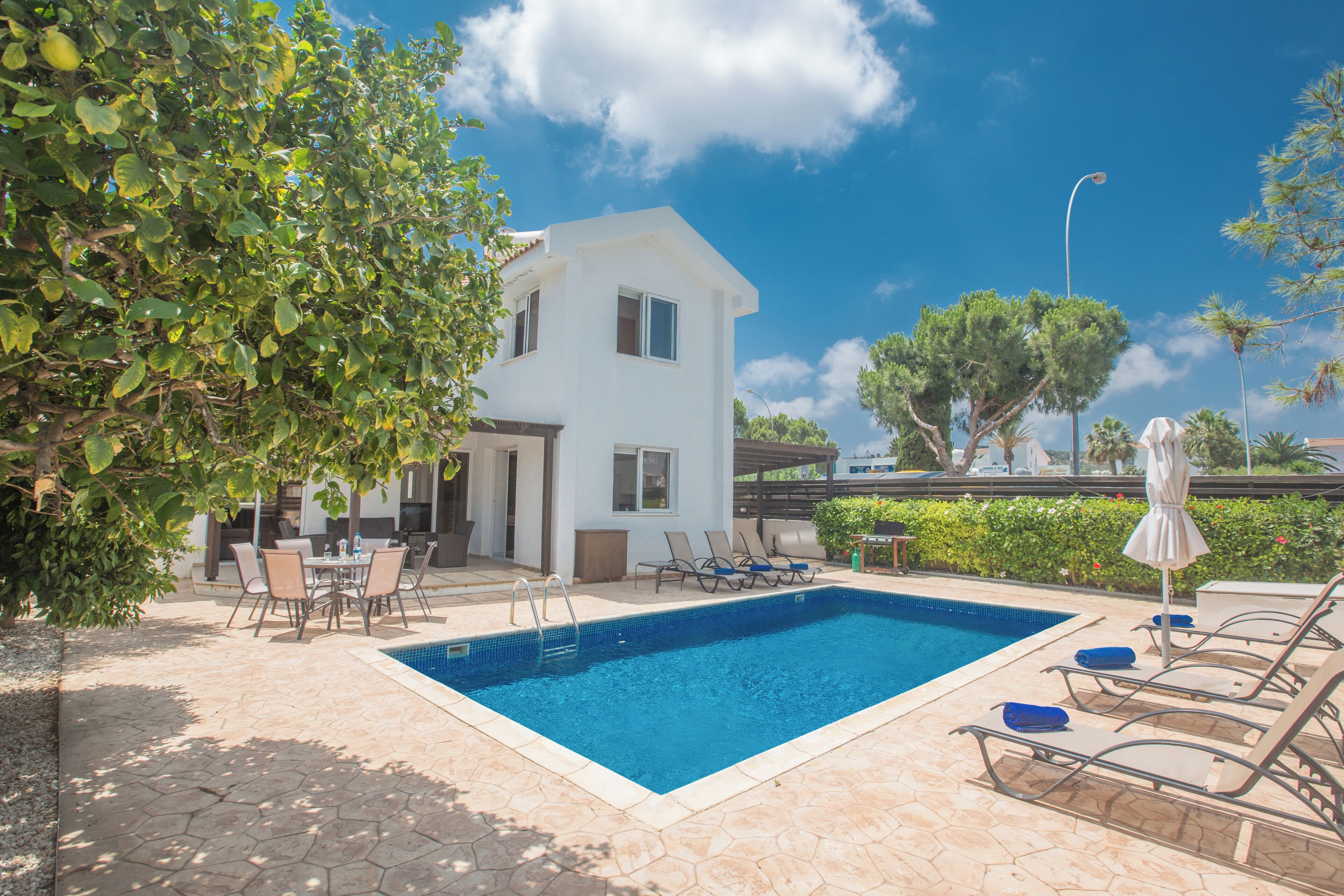 A swimming pool with lounge chairs, a dining table, and a white building with a balcony.