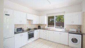 A modern kitchen with white cabinets, a microwave, oven, and a washing machine. - Protaras Holiday Villa Ma14 (Paralimni)