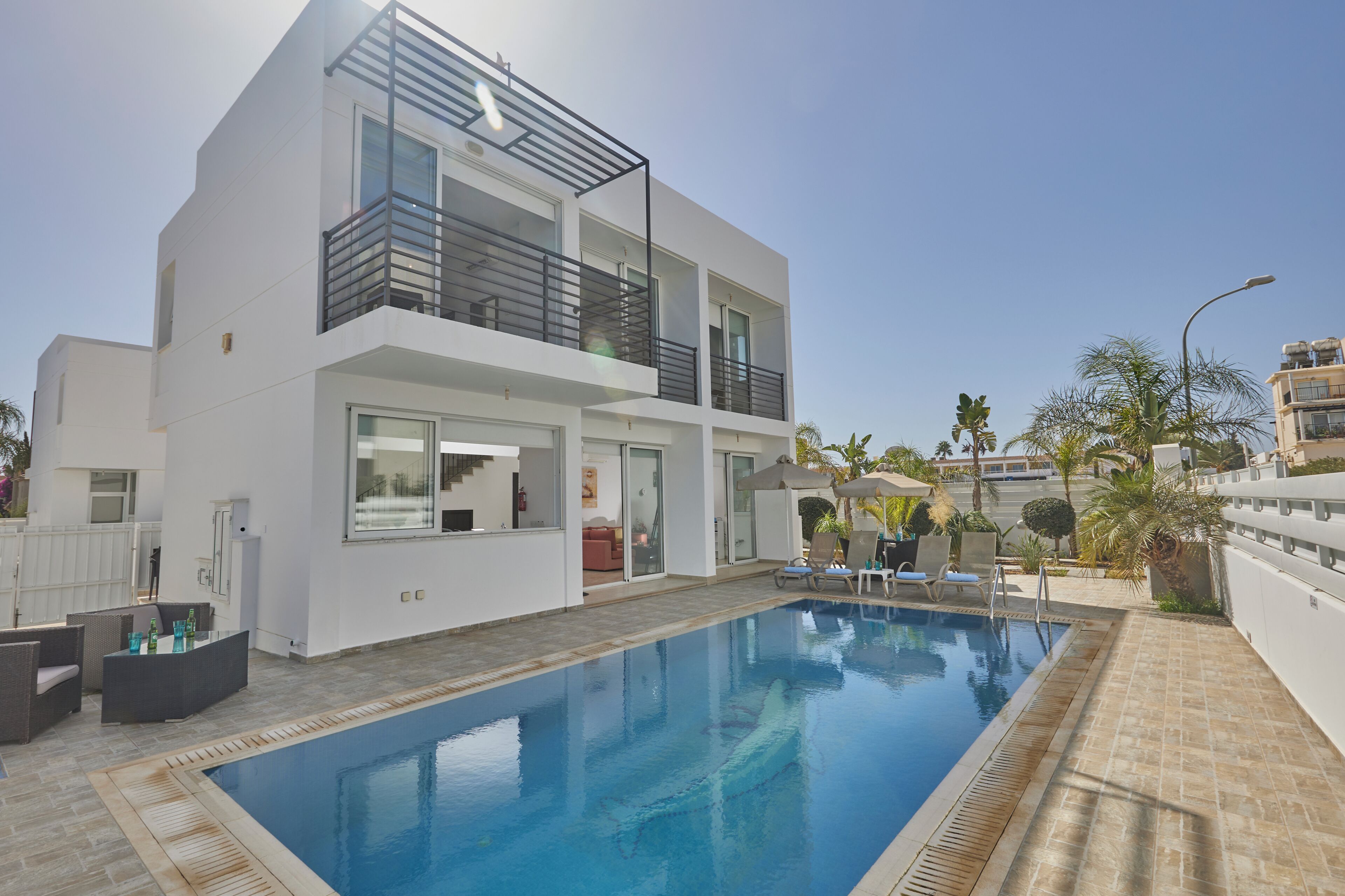 A modern two-story building with a swimming pool, outdoor seating, and a balcony.
