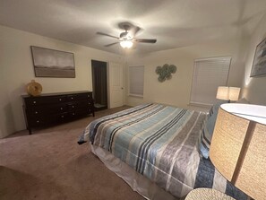A bedroom with a bed, dresser, ceiling fan, and a door leading to a closet.