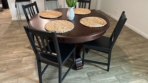 Une table à manger avec quatre chaises, un vase rempli de fleurs jaunes et des sets de table en fibres tressées.
