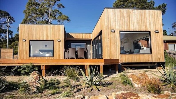 A modern wooden house with large windows and a deck.