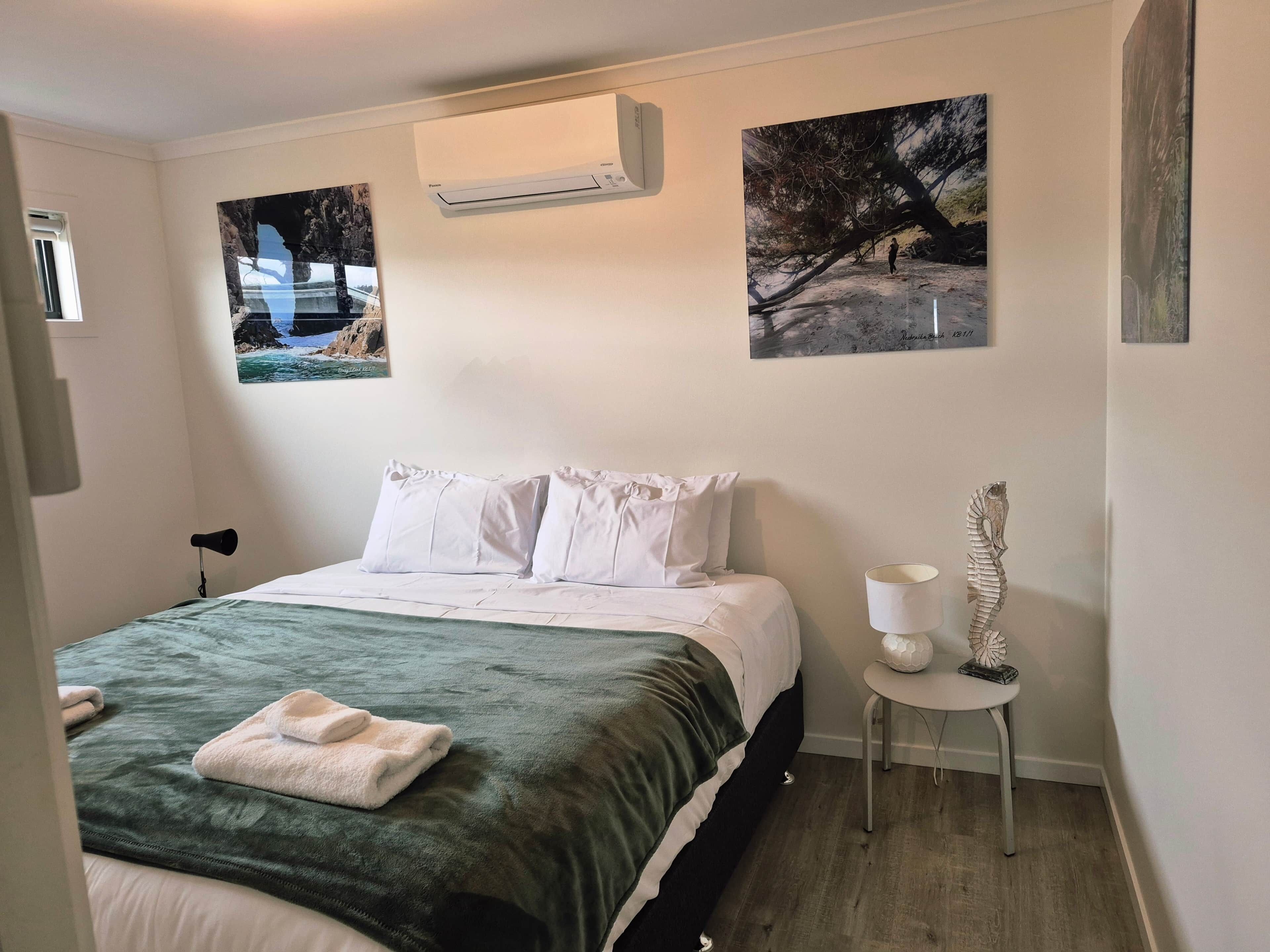 Una camera da letto con un letto, cuscini bianchi, una coperta verde, un condizionatore d'aria a parete e due quadri incorniciati.