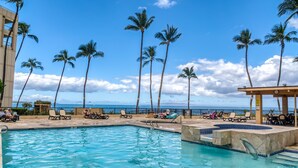 A pool area with lounge chairs and palm trees, overlooking a body of water.