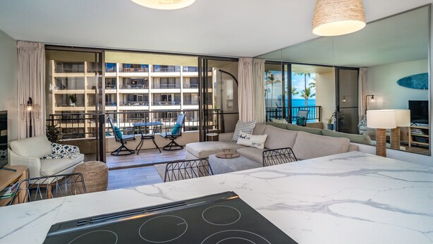 A modern hotel room with a large window, a sofa, a dining table, and a kitchen area.