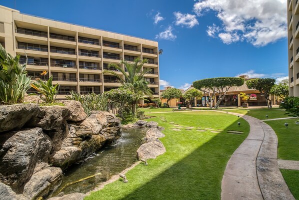 A courtyard with a small water feature, a well-maintained lawn, and a multi-story building with balconies.