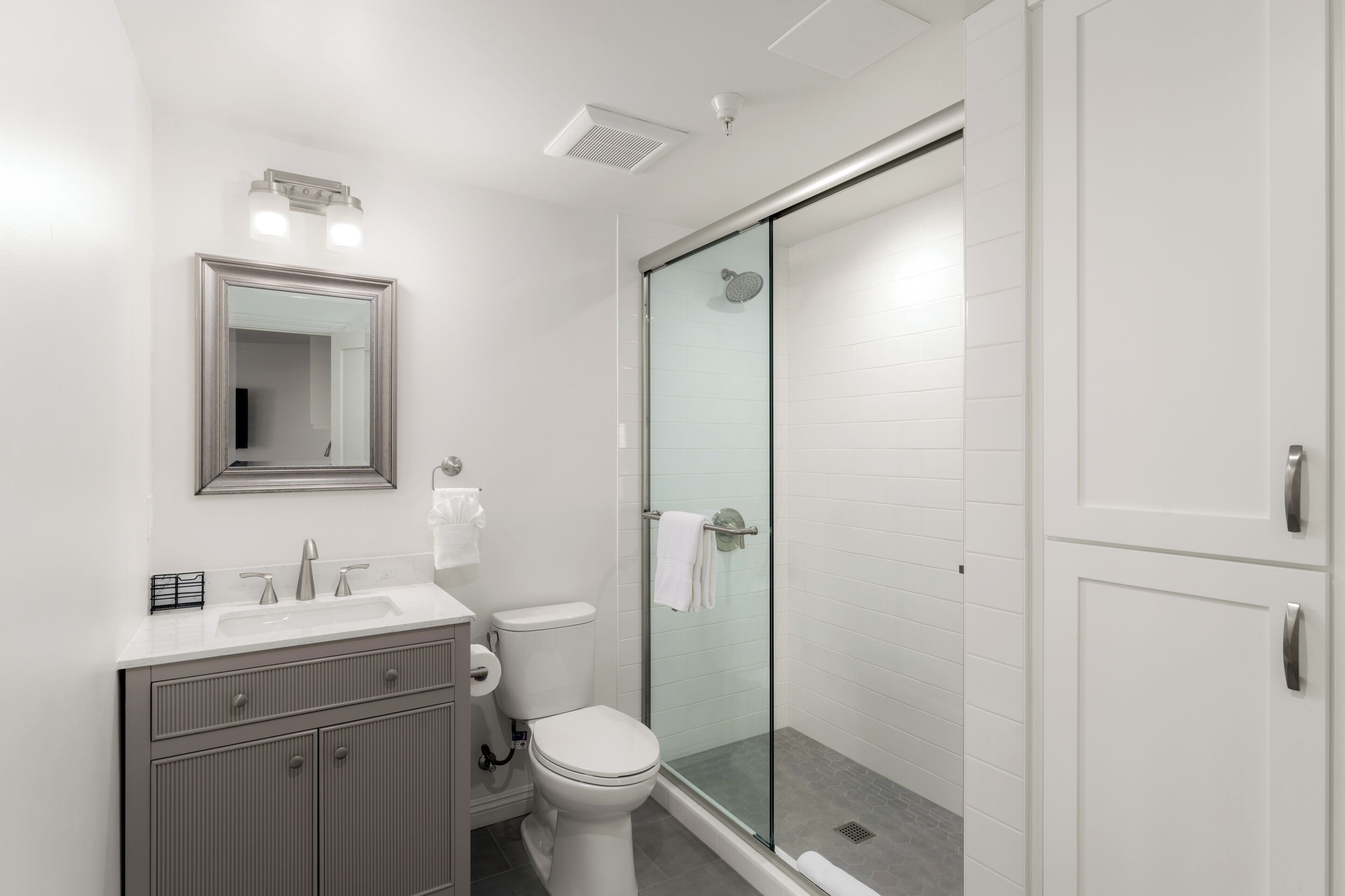 A modern bathroom with a glass-enclosed shower, a toilet, a sink with a vanity, and a mirror.