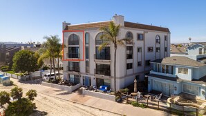 A multi-story residential building with a flat roof, large windows, and a balcony. - Large Waterfront | Private Roof Deck | Fireworks View (San Diego)
