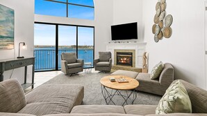 A spacious living room with a large window, a fireplace, and a flat-screen TV. - Large Waterfront | Private Roof Deck | Fireworks View (San Diego)