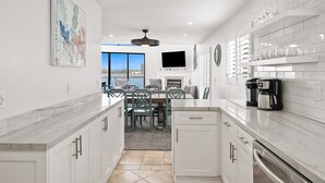 A modern kitchen with white cabinetry, a marble countertop, and a dining area with a view. - Large Waterfront | Private Roof Deck | Fireworks View (San Diego)