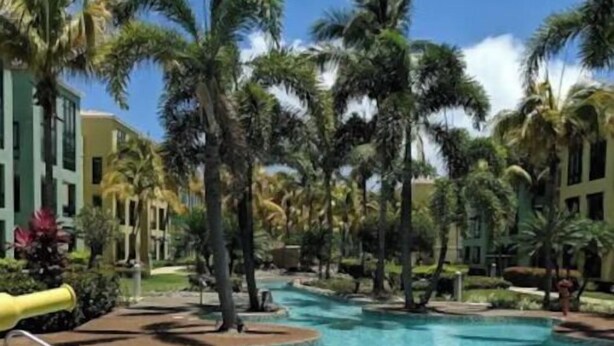 Zona de piscina con varias piscinas, palmeras y un edificio al fondo.