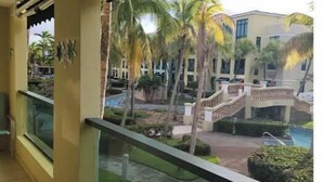 Un balcón con vistas a una zona de piscina, palmeras y un edificio con escaleras.