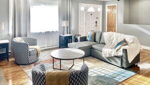 Ein modernes Wohnzimmer mit einem Ecksofa, einem runden Couchtisch und gemusterten Sessel.