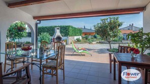 A patio area with a glass table, wooden chairs, and a barbecue grill.