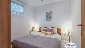 A bedroom with a bed, nightstands, a ceiling fan, a window with curtains, and a painting on the wall.
