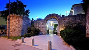 An entrance with a stone archway leading to a building, surrounded by stone walls and greenery.