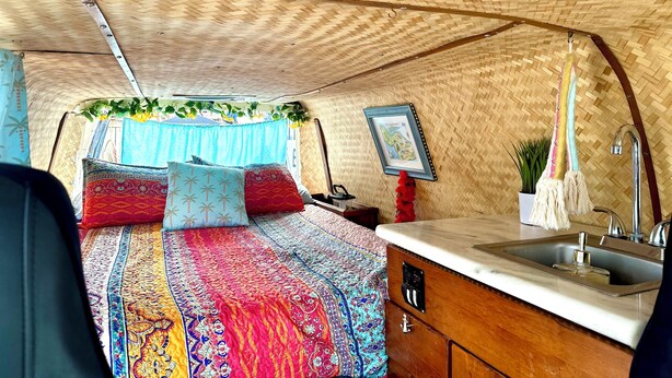 Ein gemütliches, helles Interieur mit einem Bett, einer kleinen Küchenzeile und einer hängenden Pflanze.