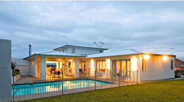 Stunning two-story home with a lawn and pool, surrounded by a secure fence.