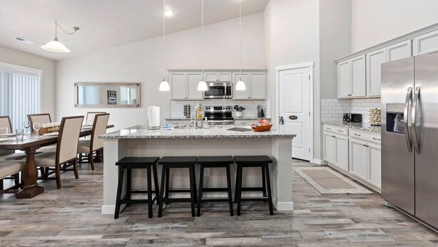 Una cocina moderna con una isla central, muebles blancos, electrodomésticos de acero inoxidable y una zona de comedor con mesa y sillas.