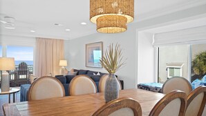A modern dining area with a wooden table and chairs, a woven pendant light, and a view of the ocean through large windows. - Gulf Front-Unobstructed Views! Book Now! (Port St. Joe)
